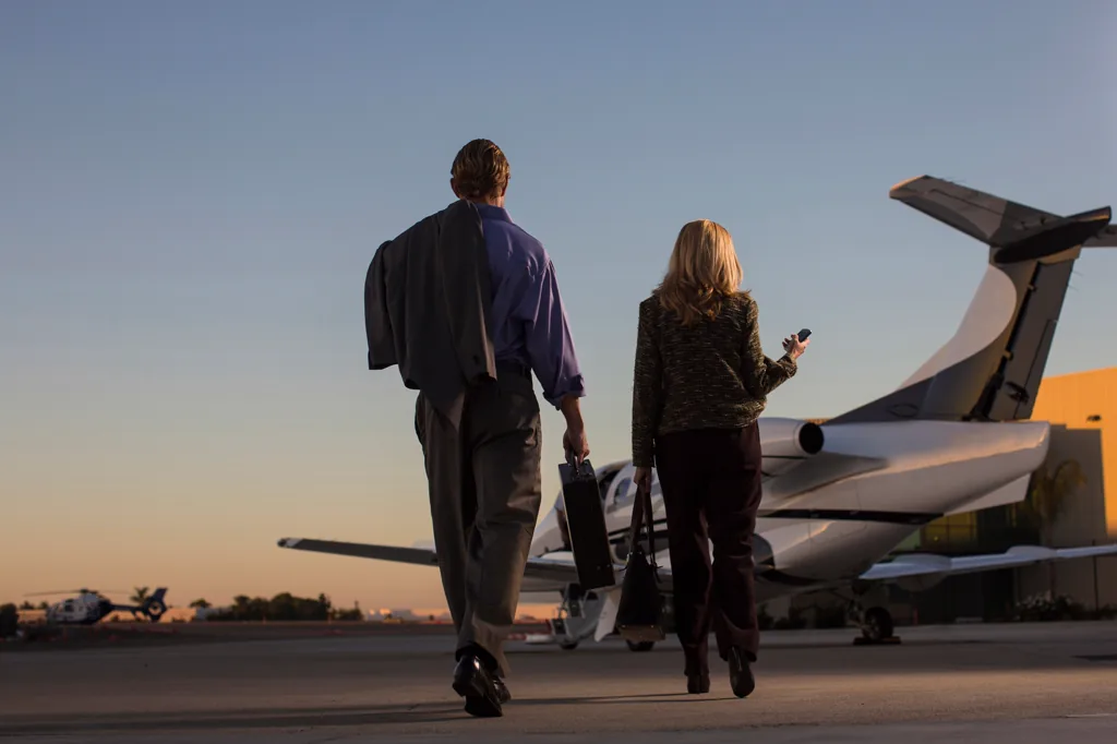 Two travellers walking on a sunlit airport runway toward a private jet